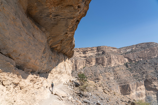 Female hiker at edge of Balcony Walk above Wadi Nakhar, Jabal Shams on sunny day, Oman