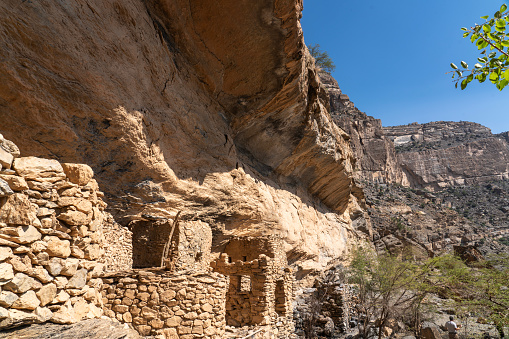 Abandoned stone houses at edge of Balcony Walk above Wadi Nakhar, Jabal Shams on sunny day, Oman