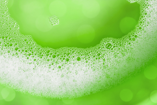 Close-up of soap suds with water on a green background. Beautiful bokeh light, space for copy.