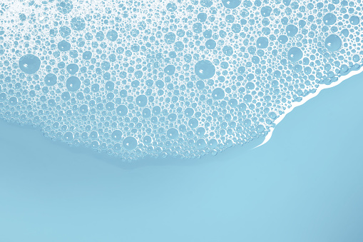 Close-up of soap suds with water on a blue background. Space for copy.