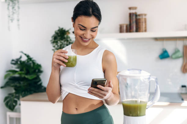 istock Pretty woman using her mobile phone while drinking fruit detox juice in the kitchen at home. 2148630205