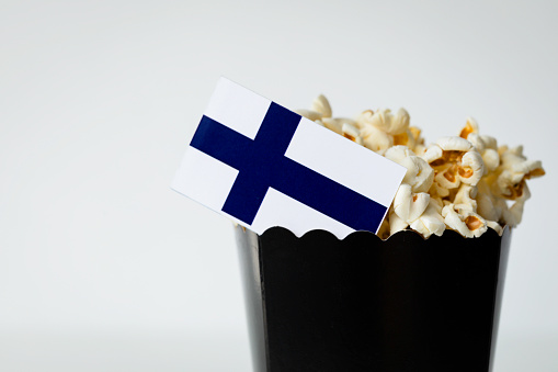 Black popcorn bag in front of white background with Finnish flag. Representing film industry in Finland.