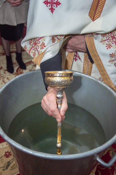 istock an orthodox priest inserts a cross into the metal baptismal vessel 2148634092