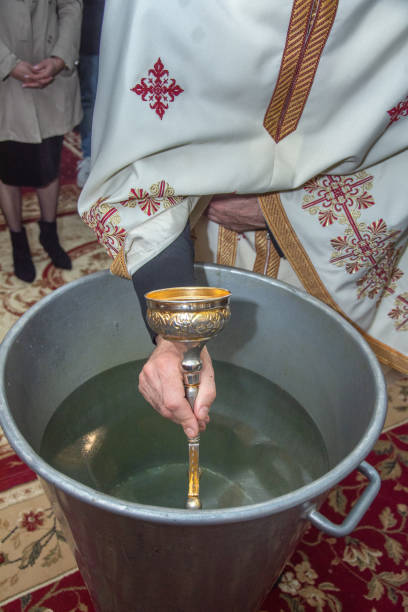 istock an orthodox priest inserts a cross into the metal baptismal vessel 2148634099