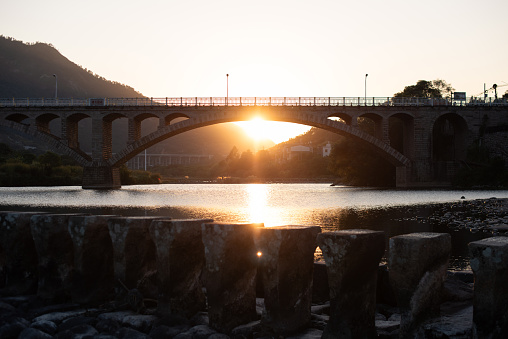 Under the setting sun, the stone bridge and stream are photographed against the light.