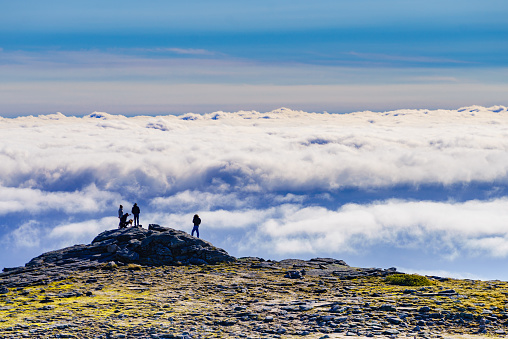 Hikers in silhouette stands on rock in mountains above clouds. Torre mountain peak, Serra da Estrela, the highest place in Continental Portugal.