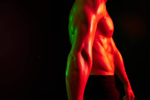 Man bodybuilder athlete posing muscle with nude torso in athletic, isolated on black background in neon light. Advertising, sports, active lifestyle, colored light, competition, challenge concept. . High quality photo
