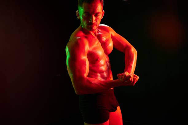istock Man bodybuilder athlete posing muscle with nude torso in athletic, isolated on black background in neon light. Advertising, sports, active lifestyle, colored light, competition, challenge concept. 2148641603