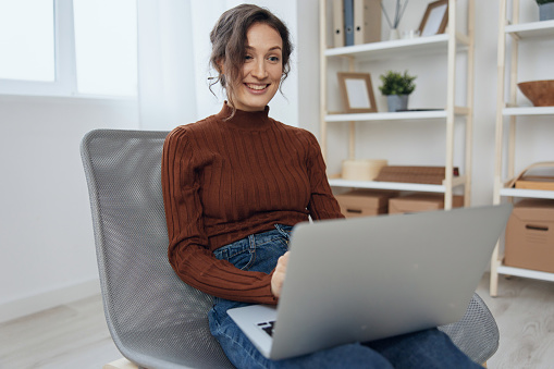 Cheerful smiling happy curly beautiful lady enjoy accepts congratulations from colleagues on video call conference using laptop loves her work sitting in chair at home. Modern Profession Remote Job