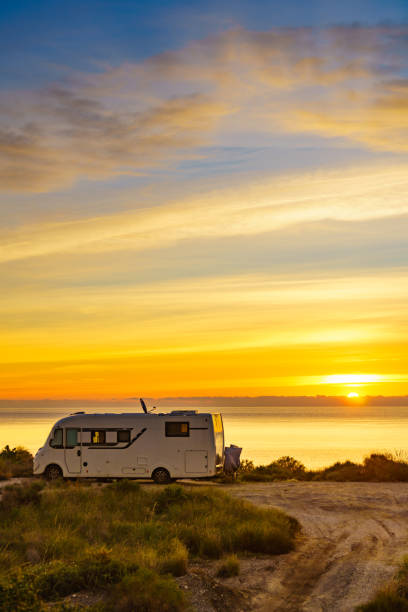 Sun rising over sea horizon and camper rv camping on beach seashore. Holidays in Spain, travel with motor home.