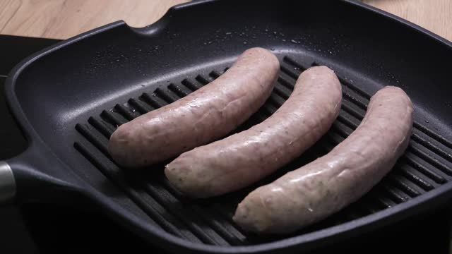 Placing Two Fresh Sausages on a Black Grill Pan.