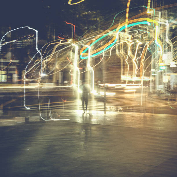 Numerous light trails lead to a man crossing a street on a bright, electric night in Shanghai