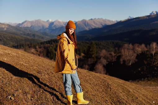 Woman smile with teeth full-length walking happiness walking on the hill and looking at the mountains in a yellow raincoat and jeans in the autumn happy journey in the sun sunset hiking, freedom lifestyle . High quality photo