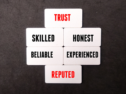 Wooden board with word TRUST,SKILLED,HONEST,BELIABLE,EXPERIENCED on black background.
