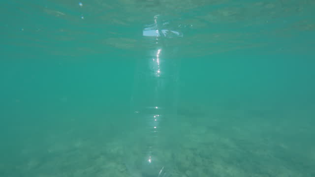Bottle is floating in the ocean upside down and is partially submerged in the water.