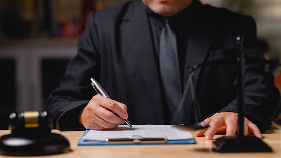 Lawyer or judge man in a suit is writing on a piece of paper. He is wearing a tie and he is in a professional setting