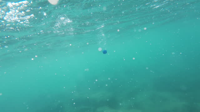 Bottle is floating in the ocean upside down and is partially submerged in the water.