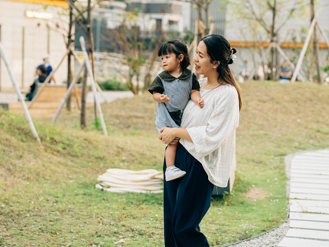 Asian mother cradles her daughter amidst the serene environment of a well-maintained park. The child, dressed in a cute outfit, gazes wide-eyed at the world around them. Their eyes, like two sparkling pools of wonder, reflect the sunlight filtering through the leaves. It’s as if they’re absorbing the magic of the moment—the rustling leaves, the distant laughter from the playground, and the gentle sway of the willow branches.
The child’s expression is a symphony of curiosity and innocence. Their tiny fingers reach out, brushing against the adult’s skin, seeking connection and understanding. Perhaps they’re pondering the mysteries of the universe—the rustle of leaves, the flight of birds, or the secrets whispered by the ancient tree.
And the adult? Their face mirrors the child’s awe. Love and protection radiate from their eyes, cradling the little one in a cocoon of safety. It’s a shared moment—a passing of wisdom from one generation to the next. The willow, witness to countless such exchanges, bends its branches in approval, as if saying, “Here, little one, let me tell you about the magic of the world.”
Together, they create a tableau—a snapshot of life’s delicate balance. The child’s wonder meets the adult’s tenderness, and in that intersection, time stands still. The willow’s leaves flutter, and the world holds its breath, honoring the beauty of this fleeting instant—a testament to the eternal dance of love and discovery.