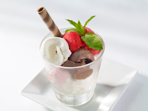 Cup of gourmet ice cream with vanilla and fruit flavor on table.