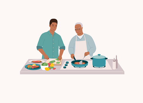 Smiling Black Elderly Father In Apron Cooking Steak With Frying Pan. Adult Son Helping His Dad To Cut The Cucumber. Isolated On Color Background.