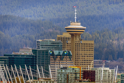 Vancouver, British Columbia, Canada. Apr 13, 2024. The captivating sight of the Harbour Centre in Downtown Vancouver set against the backdrop of lush mountain forests during the afternoon hours.