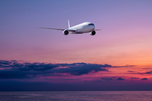 Wide body passenger airplane is landing over the sea against the backdrop of picturesque sunset sky