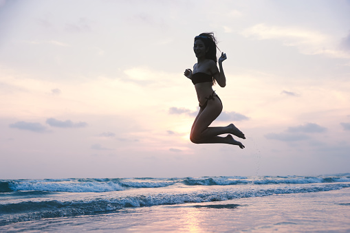 Enjoy Happy Woman running and arm raise and jump on the tropical beach on summer vacation, enjoy summer vacation against a sunset sky