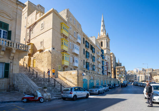 Editorial Malta scene featuring a tall church spire and classical stone architecture set against a vivid blue sky. Captures historic European cityscape, architecture, and religious heritage. Malta, Valleta