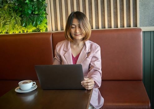 woman wearing suit pink sitting in the cafe and using laptop working check email and planing business freelance concept