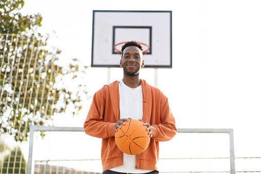 Portrait of a young african american basketball player posing next to basketball hoop