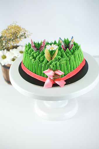 A cake adorned with grass and flowers is presented on a plate.