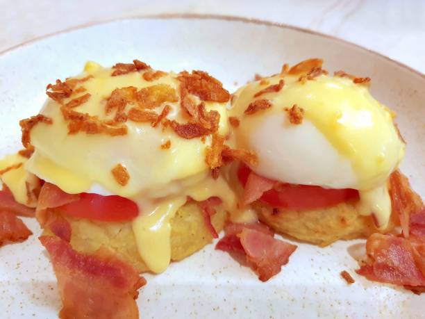 istock Eggs Benedict. Two poached eggs on potato pancakes or toasted bread with tomatoes, fried onions and bacon with hollandaise sauce. Delicious hearty breakfast, restaurant serving dishes. Close-up 2148665770