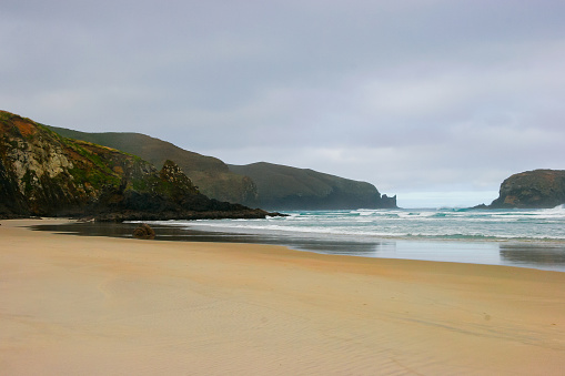 Flat sand beach with mountains in the distance on an overcast day in the Otago peninsula near Dunedin
