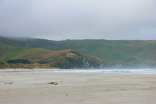 Flat sand beach with mountains in the distance on an overcast day in the Otago peninsula near Dunedin