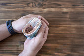 Man's hand holding a bundle of money on a wooden background.
