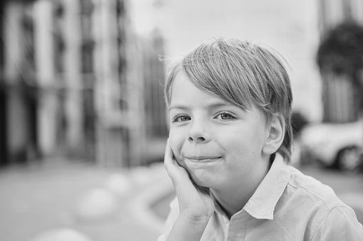 Handsome smiling little boy on the sunny urban background . Close-up portrait. Blond hair, blue eyes , 9 years boy smiling, having fun in the city. High quality photo