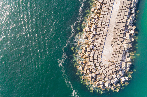 Top view with drone of a breakwater with large boulders jutting into the sea. Surrounded by a calm sea. Ideal for backgrounds or travel concepts