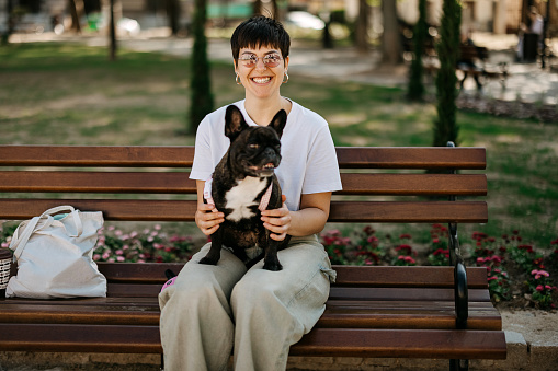 Woman sits on her dog on a park bench