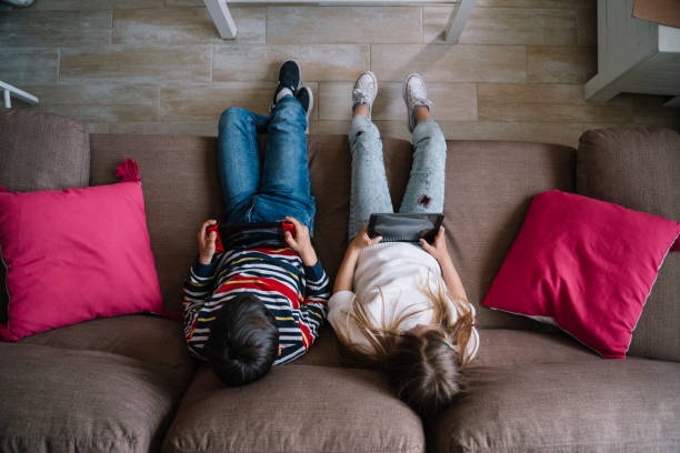 Curious kids watching videos or playing games on a mobile phone while sitting on the couch