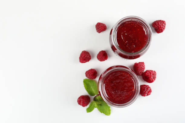 Jars of raspberry jam with ingredients on  white background