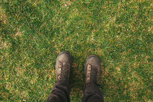 Top view of male feet in boots standing on green grass lawn with copy space