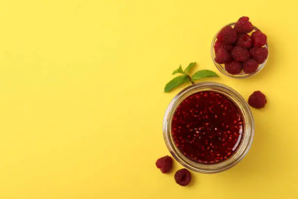 Photo of Jar of raspberry jam with ingredients on yellow background