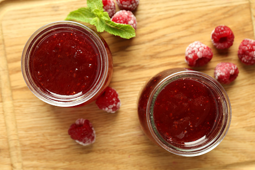 Glass jars of raspberry jam with ingredients on wooden board