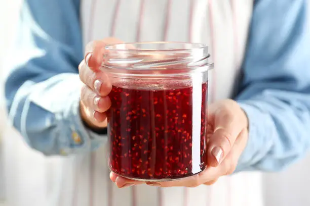 Photo of Woman holding jar of raspberry jam in hands, close up
