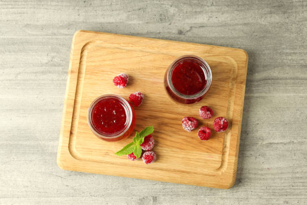 istock Glass jars of raspberry jam with ingredients on wooden board 2148672763