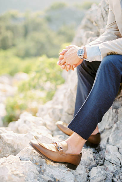 Groom sits on a rock with his hands folded in his lap. Cropped. Faceless. High quality photo