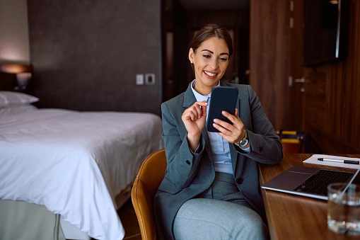 Happy businesswoman using smart phone while being in a hotel. Copy space.