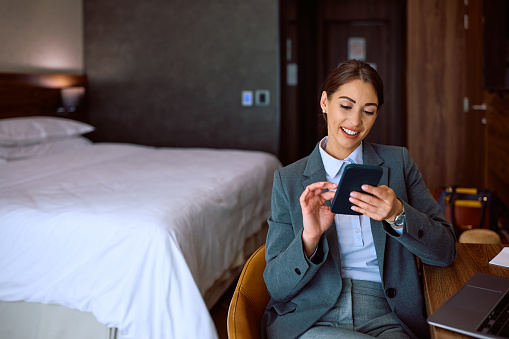Happy businesswoman texting on mobile phone in hotel room. Copy space.