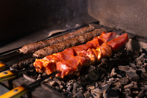 Close-up of an appetizing kebab or shashlik made of fresh meat and lula kebab is cooked on a charcoal grill with smoke.