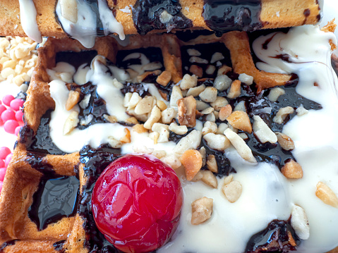 Close-up of waffles with fruit pieces, cherries, chocolate sauce and toffee sprinkles